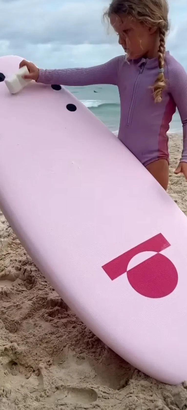 Child with a pink surfboard on a beach